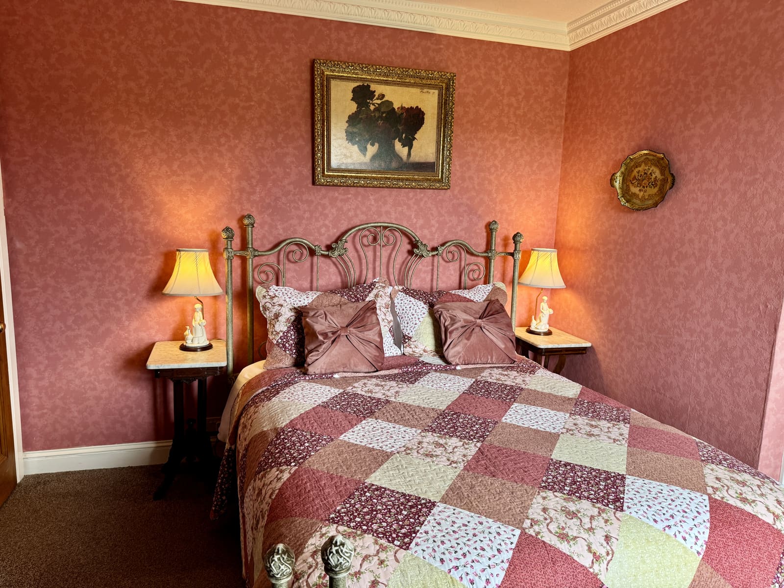 King Ensuite with rose wallpaper, bedside lamps, and a patchwork quilt