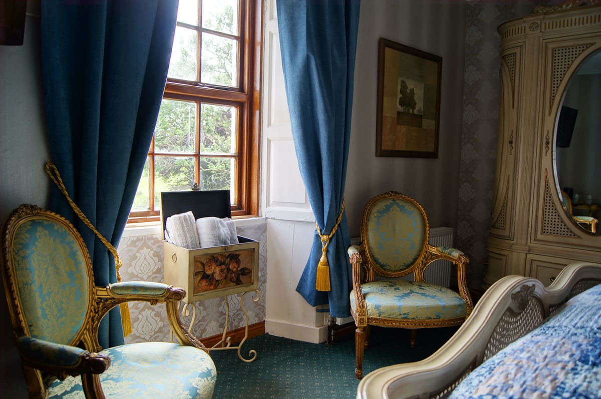 Family Ensuite seating area with blue curtains, antique chairs, and a window overlooking the grounds