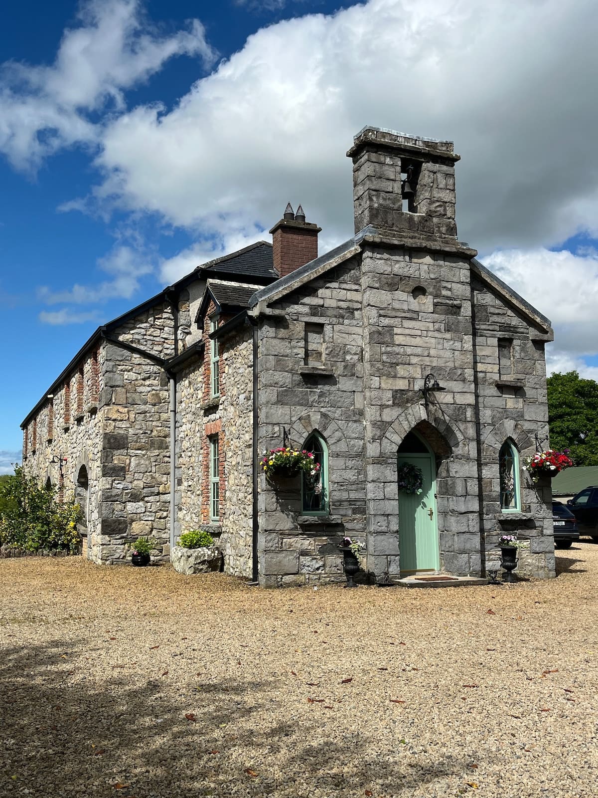 Stone self-catering cottage with pointed-arch doorway, sage-green door, and hanging flower baskets