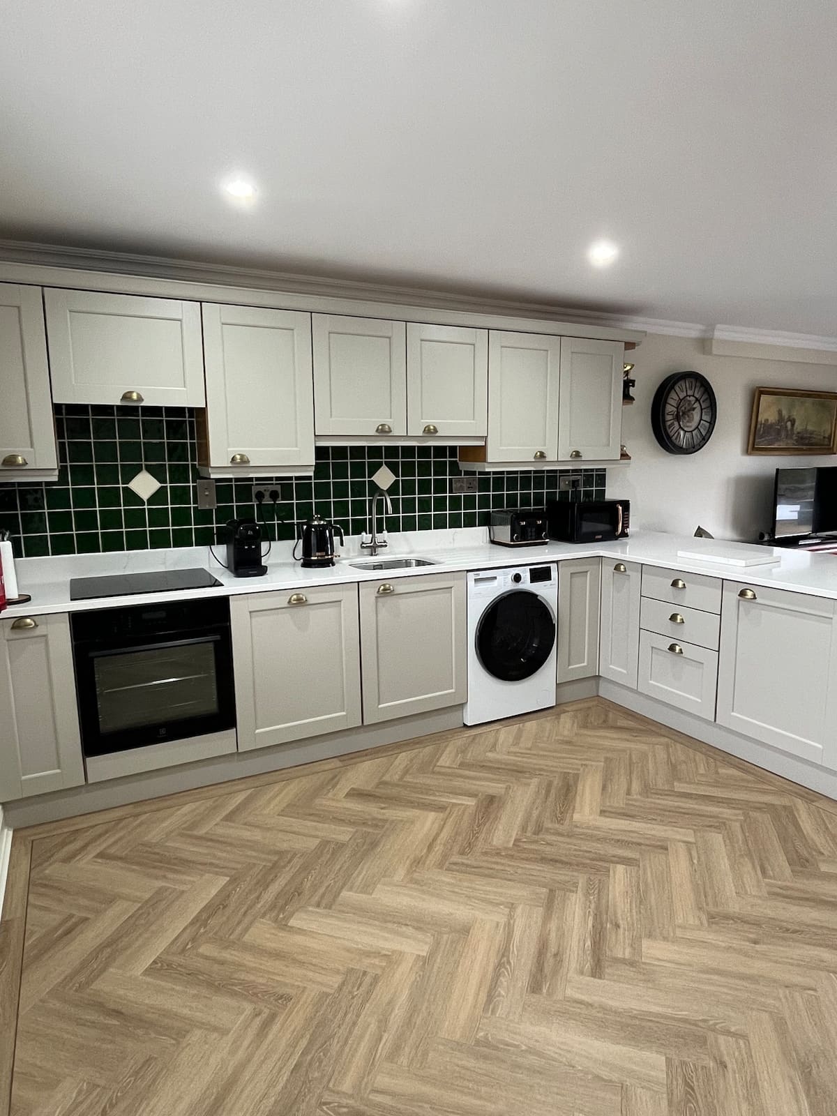 Fully equipped kitchen with green tiled backsplash, induction hob, oven, and washing machine