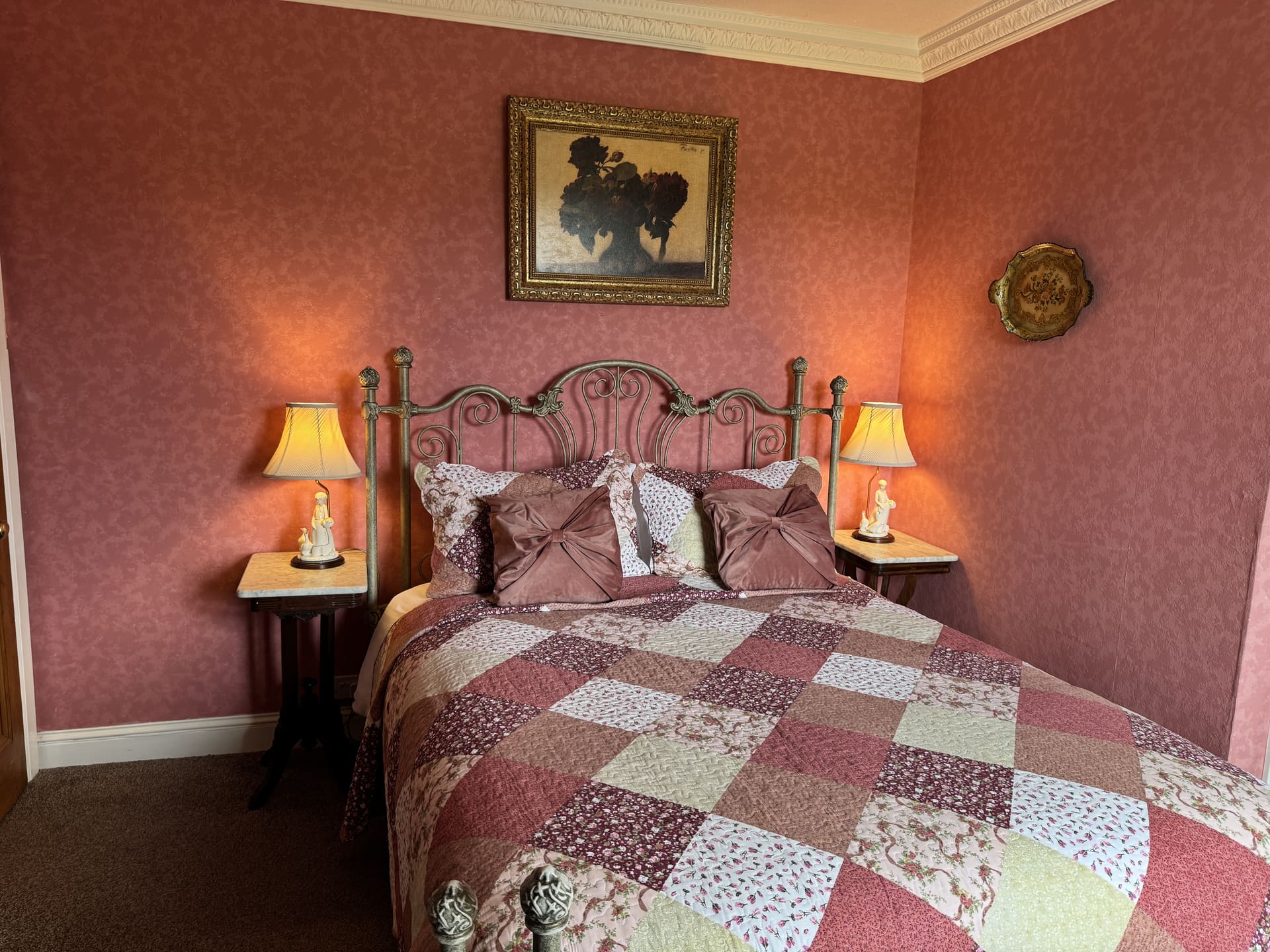 Antique iron bed with patchwork quilt against pink walls